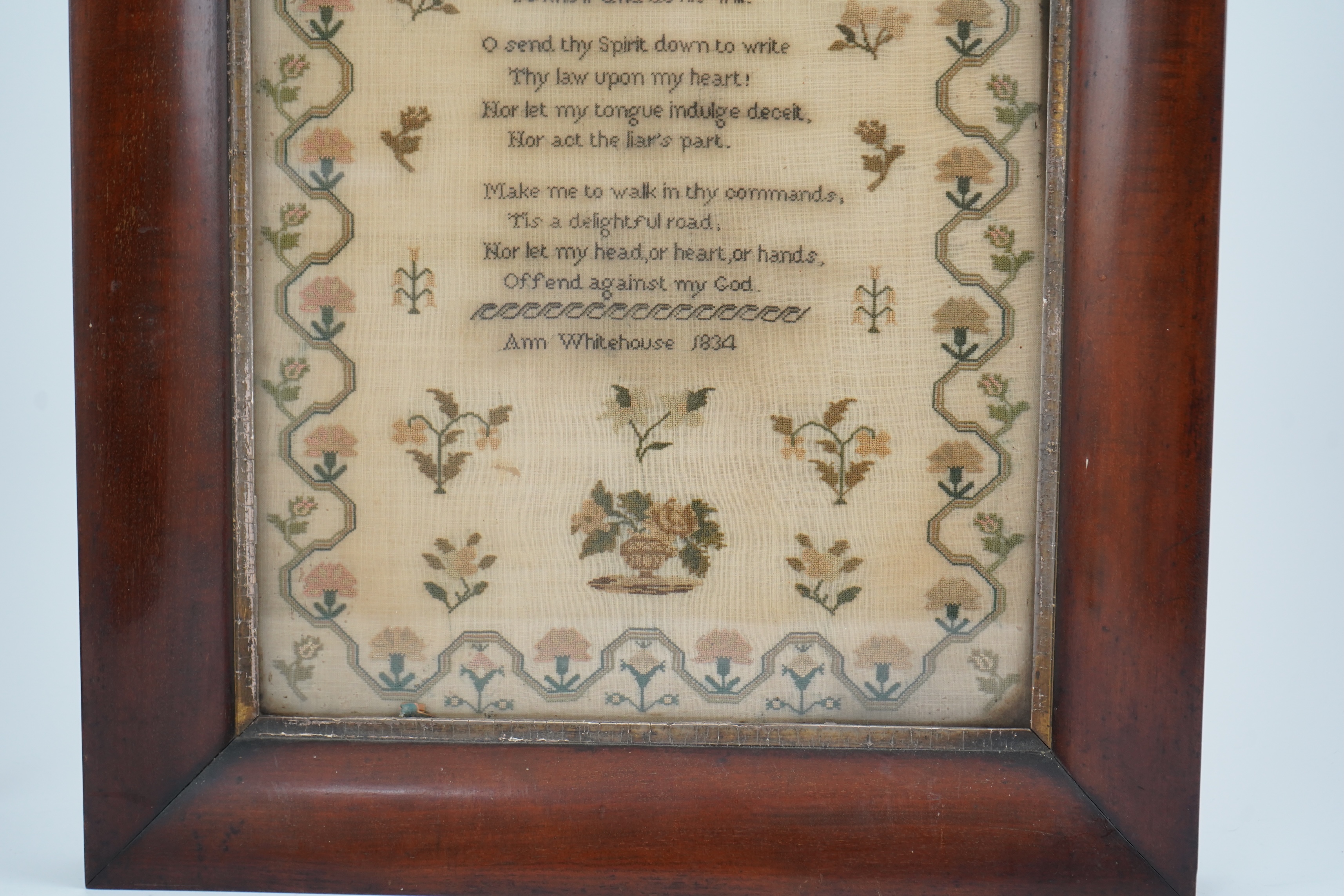 A wide mahogany framed sampler by Ann Whitehouse dated 1834, worked in coloured silks on a fine linen ground, in small stitches, bordered with a geometric stylistic vining pattern, set with a central verse, above her nam